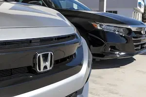 Close-up of Honda badge and grille on a silver Honda vehicle at a dealership lot.