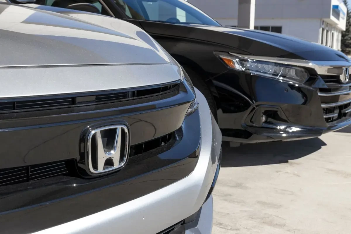 Close-up of Honda badge and grille on a silver Honda vehicle at a dealership lot.