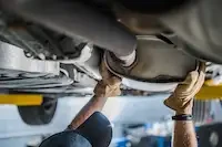mechanic inspecting a catalytic converter from underneath