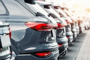 A row of new SUVs parked at a car dealership lot, shown from behind, with taillights and reflective bodywork visible in the foreground.