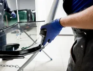 gloved hand applying adhesive to windshield edge on a glass stand