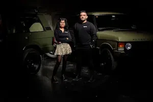 Two people in black Revv-branded sweatshirts stand in front of a green Range Rover in a dark garage.