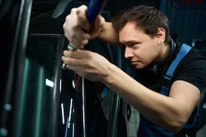 A collision repair technician uses a straightening tool on a vehicle body panel in an auto body shop.