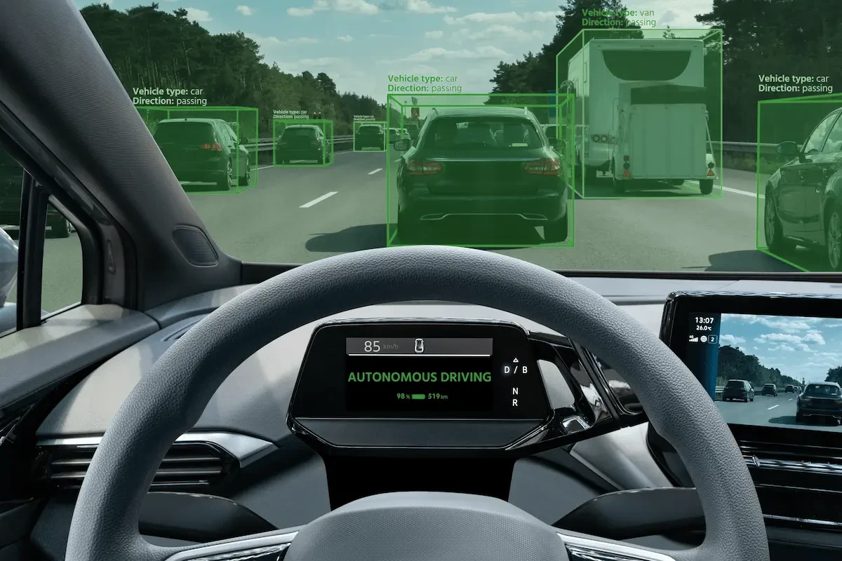 A view from a vehicle's driver's seat shows an instrument cluster reading "Autonomous Driving" as detection boxes outline surrounding vehicles on a highway.