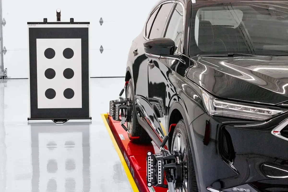 A black Acura SUV on a red Hunter alignment rack with wheel-mounted sensors, positioned in front of a Hunter Ultimate ADAS calibration target board in a clean, well-lit shop.
