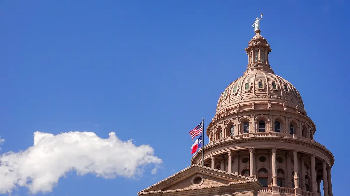 The Texas State Capitol building in Austin, its dome and columned entrance visible under a blue sky.