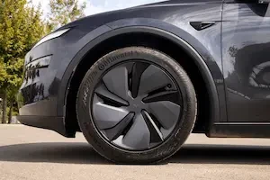 Low-angle close-up of a dark gray Tesla Model Y's front wheel and fender, showing a black multi-spoke wheel with a Continental tire, parked outdoors near trees.