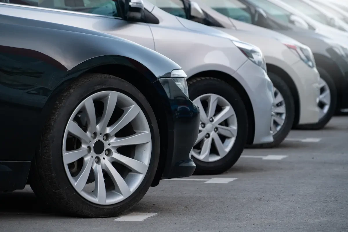 Close-up of front wheels and fenders of several parked cars lined up in a row, with white parking space markings visible on the pavement