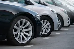 Close-up of front wheels and fenders of several parked cars lined up in a row, with white parking space markings visible on the pavement