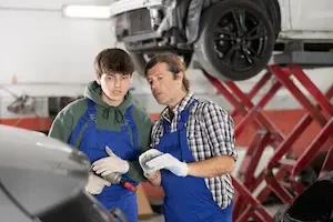 Young mechanic consulting with experienced technician in auto repair shop