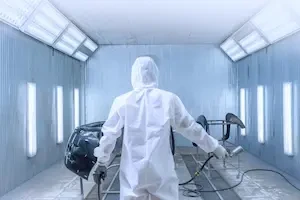 A collision repair technician in a protective coverall and respirator sprays paint inside a booth.