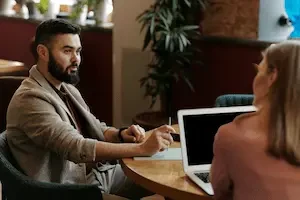 man sitting at a table next to a woman on a laptop