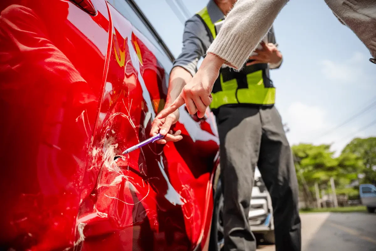 red vehicle with dent in side and two people pointing at it