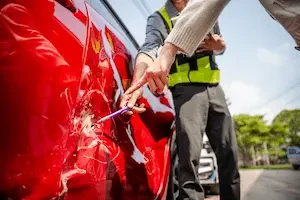 red vehicle with dent in side and two people pointing at it