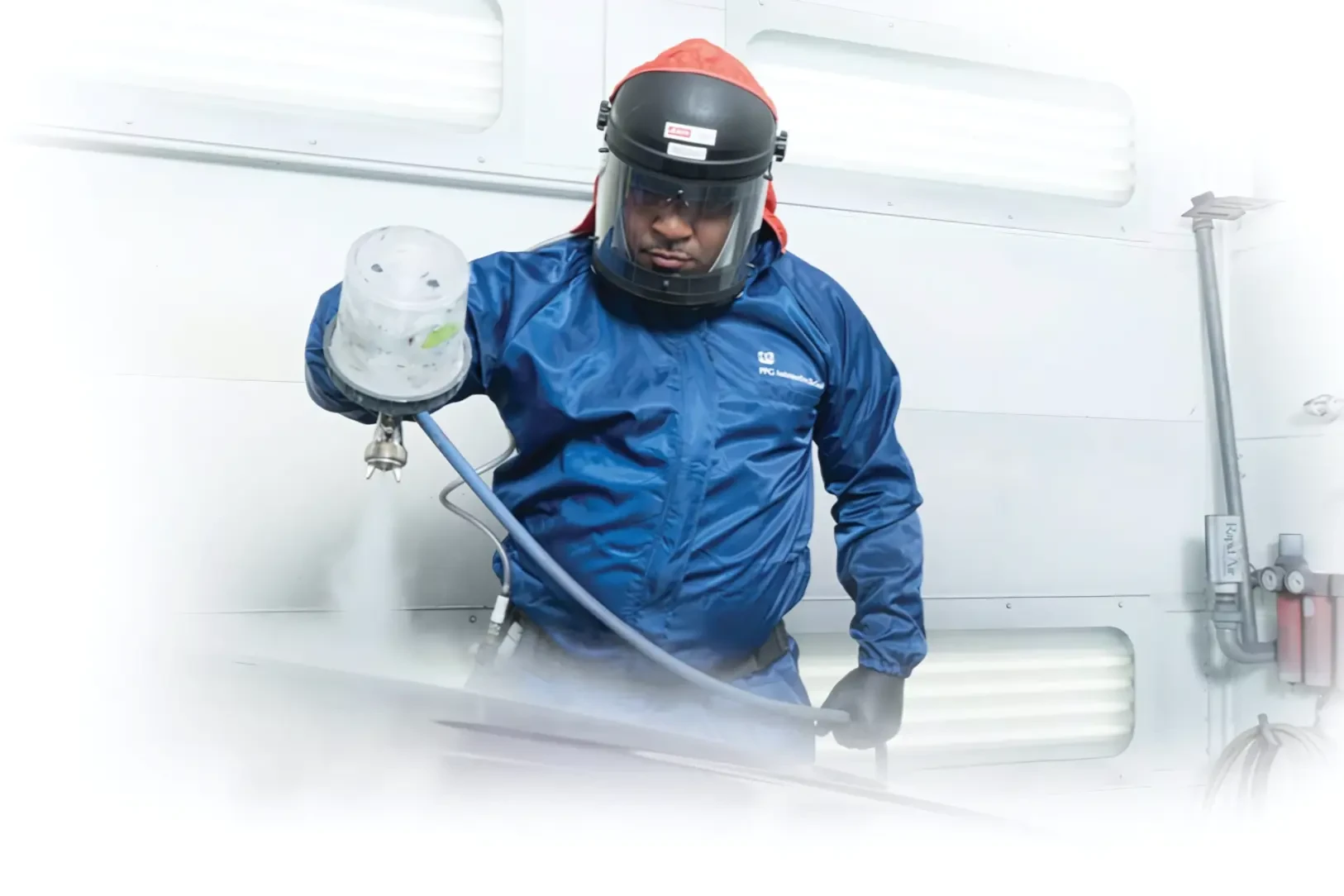 Man in blue PPE suit and full face mask spraying a clearcoat on a car in a paint booth