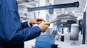 closeup of mechanic holding a table in a repair shop with a car on a lift in the background