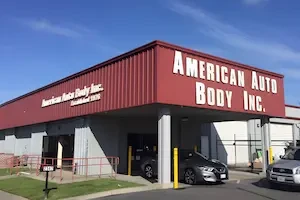 Exterior of white rectangular building with a red roof that reads American Auto Body Inc. on the front and American Auto Body Inc. Established 1976 on the side.