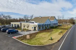 exterior shot of a large gray building with gray shutters on top and a large 3 bay garage on the far front side for cars.