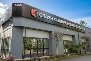 Exterior of a rectangular gray building with large windows and a large black sign that says Crash Champions