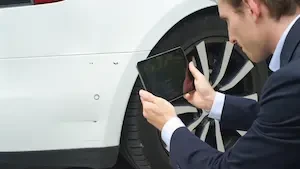insurance adjuster holding a small screen next to a car