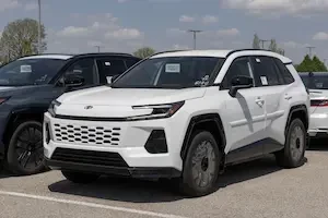 A white Toyota RAV 4 SUV model year 2026 sitting in a dealership lot outdoors next to a dark SUV.